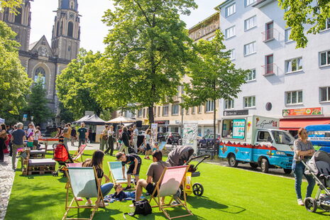 Das Bild zeigt Menschen, die in Liegestühlen auf dem Stiftsplatz sitzen.